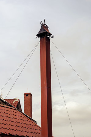 A red roof with a chimney against an overcast sky. The tall chimney with the cap is whisked by metal stretchers. Architecture.の写真素材