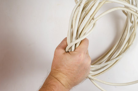 A man is holding a roll of old white wire against a white background. The old wire is a twisted...