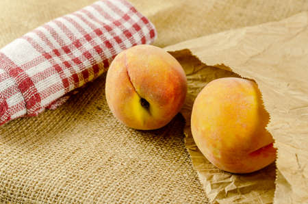 Ripe peaches on sackcloth. Two red fruits. Checkered fabric. Paper bag. Close-up. Selective focus.の写真素材