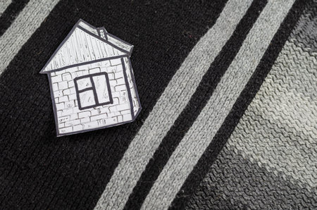 A paper house in black and gray wool. A drawing of a house with a roof, window and door drew on white paper. Knitted neck scarf. Home comfort concept. Top viewの写真素材