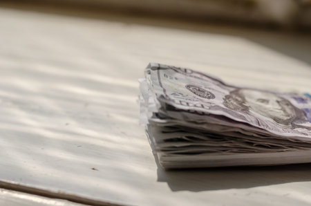 A defocused shot of a wad of crumpled money on a white wooden table. One hundred American dollars....