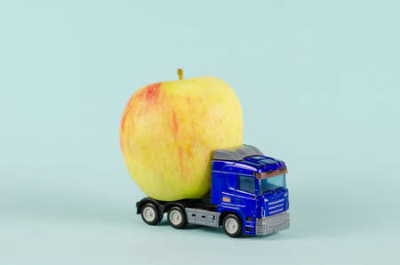 Toy truck pulling a ripe apple. Blue plastic truck with fruit against the blue background.の写真素材