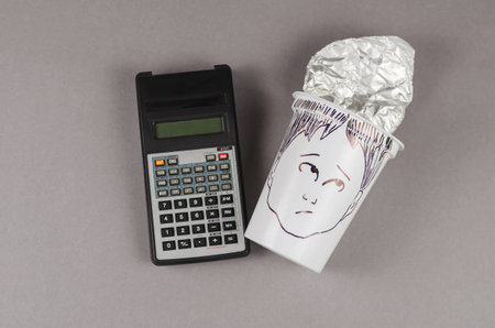 Calculator and a surprisingly human face painted on the plastic cup. White empty cup with a foil lid. Business concept, accounting, calculations.の写真素材