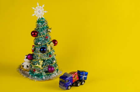 Toy truck carrying boxes of Christmas presents. Blue car with colorful boxes. Christmas tree on yellow background.の写真素材
