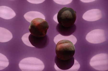 Geometric composition with peaches and round shadows. Three ripe fruits on a pink background. Side view at an angle. Selective focus.の写真素材