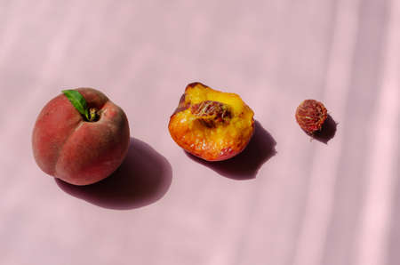 Minimalist composition with peaches on a pink background. Ripe, bitten peach and pit in a row. Three different stages of eating the fruit. Side view from an angle. Selective focus.の写真素材