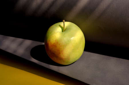 A ripe apple on a gray-yellow background. Ready-to-eat fruit in bright sunlight. Close-up. Selective focus.の写真素材