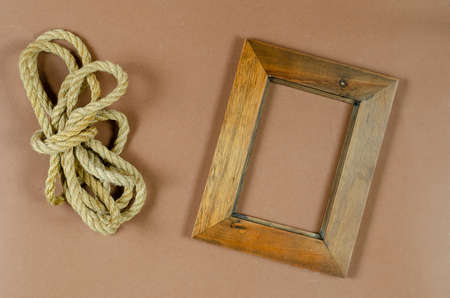 An empty photo frame and a roll of rope on a brown background. A wooden picture frame. Natural cord. Top view.の写真素材