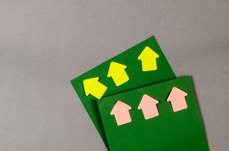 Square sheets of paper and bookmark arrows against a gray background. Green paper, pink and yellow arrows. Top view.の写真素材