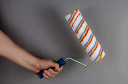 New paint roller and hand on gray background. Man holding hand tool for painting walls, ceilings, furniture and other surfaces. Painting services. Side view.の写真素材