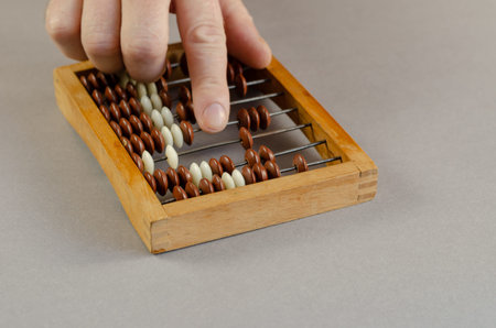 Right hand of an adult male performs mathematical calculations on wooden abacus. Indoors. Close-up....