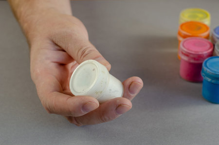 A man is holding white gouache paint in his hand. A cylindrical plastic container with paint....