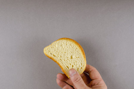 A hand holds a slice of wheat bread. An adult man and a slice of bread against a gray background....