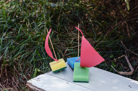 Three homemade toy ships on a white park bench. Childrens sailboats made from kitchen sponges....