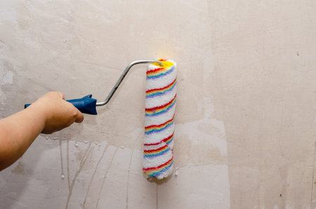 A woman holds a paint roller and impregnates the walls of the room with a primer. Preparing the...