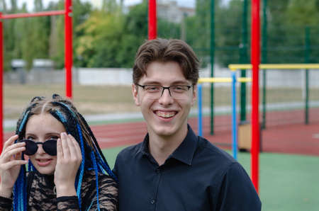 Laughing happy young woman and young man in front of a sports field. Heterosexual couple in love outside. Young adult date. Woman with blue pigtails. Man wearing optical glasses. Love, romance.の写真素材