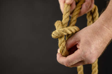 An adult male is spooling rope against black background. Hands untie knots on yellow burlap rope. Close-up. Selective Focus.の写真素材