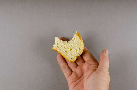 A hand holds a bitten half of a slice of wheat bread. A adult man and a slice of bread against a gray background. Top view.の写真素材