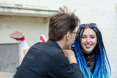 A happy young family in love. Man looking at woman lying on concrete parapet with tongue out. The female with long blue pigtails grimaces. Love, relationships. Selective focus.の写真素材