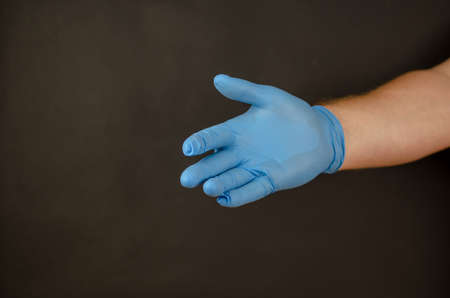 Hand of an adult male wearing a blue medical glove against a black background. Side view. Health and Medicine.の写真素材