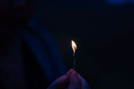 The flame of a small burning match in a womans hands. Woman protects the fire from the wind. Dusk, shooting outdoors. Blur, noise, defocus, grain effect.の写真素材