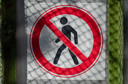A sign prohibiting access to the fence. Gray fence with a red and white prohibition sign. Shadows of the wire mesh on the fence.の写真素材
