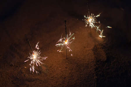 Beach sand at night with Bengal lights. Sparks of bright Bengal lights burning on the beach against the sea. Romantic nighttime background. Defocus, blur, noise, grain effect.の写真素材