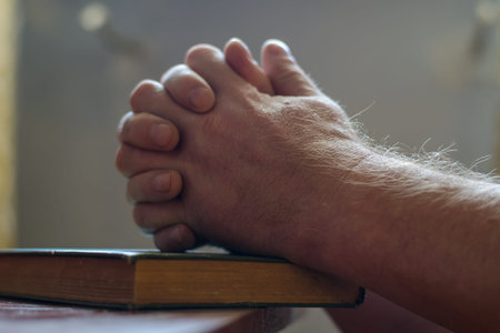 A defocused shot of two men's hands over a closed book. Palms folded for prayer. Hardcover book....