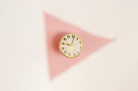 Vintage clock in a blurred white triangle on a pink background. Round Mechanical table clock in...