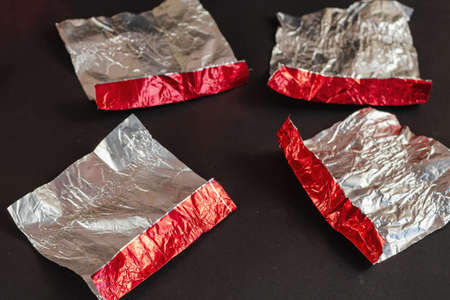 Empty red and silver candy wrappers on a black background. Crumpled foil from chocolate treats. Selective focus.の写真素材