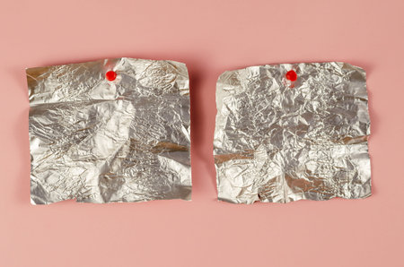 Two Empty candy wrappers pinned to a pink background. Rectangular pieces of crumpled foil...
