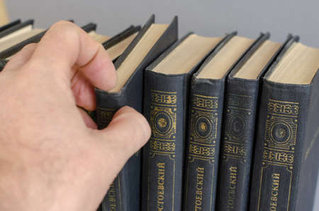 A man takes a book by Fyodor Dostoevsky from the bookshelf. A multi-volume collection of works by the famous Russian writer. Ukraine, Mykolaiv - 10 11 2021のeditorial素材