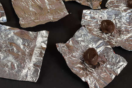 Round chocolate candies and empty wrappers on a black background. Crumpled silver foil with chocolate treats. Selective focus.の写真素材