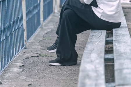 Lower section of female sitting on bench. Female in wide black pants, white shirt and athletic shoes. Side view. Selective focus.の写真素材