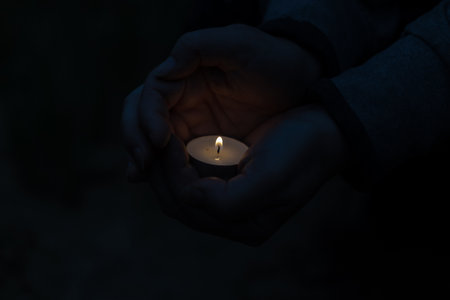 The flame of a small burning candle in a woman's hands. The woman protects the burning wick from the wind. Dusk, shooting outdoors. Blur, noise, defocus, grain effect.の写真素材