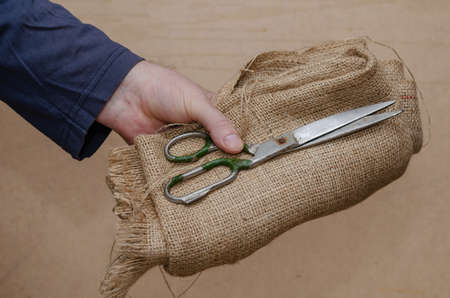 Old scissors, sackcloth in hand. A grown man's hand holds the rough cloth and old scissors. Close-up. Selective focusの写真素材