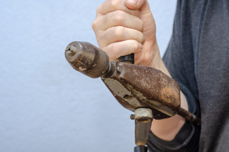 A man holds an old manual drill in his hand. A rusty metal hand tool. Close-up. Selective focus.
