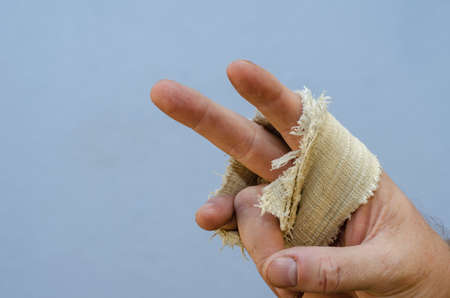 Gesture of victory. Man's hand wrapped with a narrow strip of cloth. Right hand of adult male against the blue background. Close-up. Selective focus.の写真素材