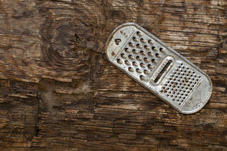 An old rusty kitchen grater on a rotting board with a knot. Top view. Copy space. Selective focus.の写真素材
