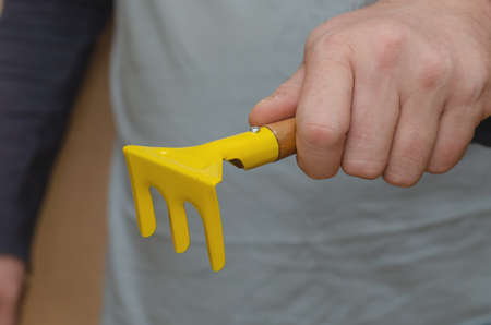 Children's garden tools. A man's hand holds a toy rake. Yellow rake with wooden handle. Indoors. Selective focus.の写真素材