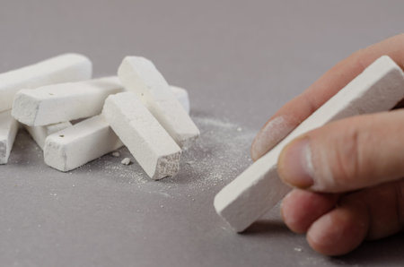 The hand of a grown man takes a piece of chalk lying on a gray background. Rectangular random pieces...