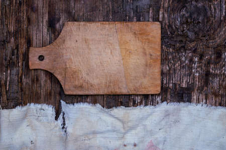 Wooden cutting board and old tattered fabric on a textured wooden background. Top view. Selected background.の写真素材
