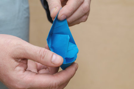 Two Hands holding a paper boat. Adult male with a blue children's boat. Close-up. Inside the room....