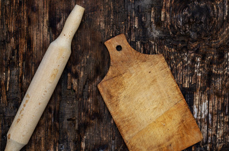 Wooden rolling pin and cutting board on a dark burnt wooden surface. Kitchen utensils. Top view. Selective focus.の写真素材