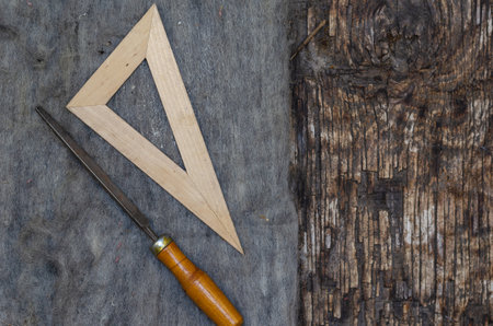 A file and a triangular ruler lie on old felt. Cracked burnt wooden background with a knot. Top view. Selective focus.の写真素材