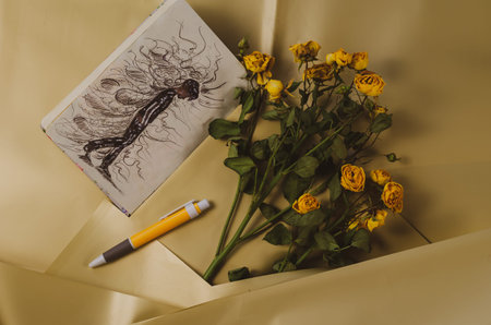 A drawing in a notebook and a fading bouquet of yellow roses. Sketch of a depressed teenager walking with his head down. Pessimistic thoughts fly around him. Selective focus.の写真素材