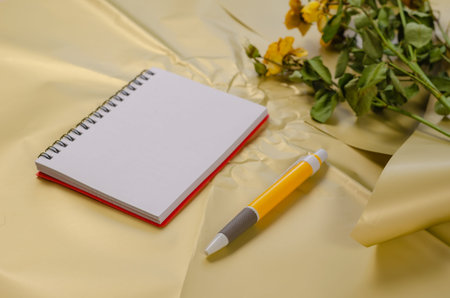 Open spring-loaded notepad with pen on cream surface. Fading Yellow Roses in the background. Selective focus.の写真素材