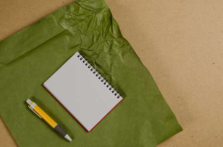 An open notebook with blank white sheets and a yellow pen against a multicolored surface. Green crumpled paper against a beige background. Top view. Selective focus.の写真素材