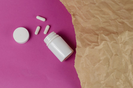 White plastic vial and medical pills against a magenta background. Medication and Torn piece of...