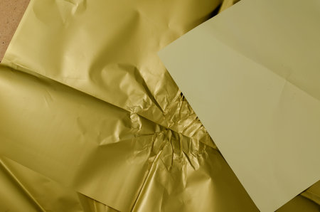 Crumpled olive-colored wrapping paper. Light beige square sheet of paper on top. Uneven surface....